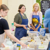 Three women in aprons working together at a table with various items.