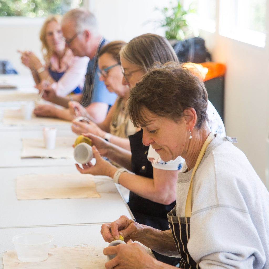 Group of people participating in a ceramics class, with one person in an apron actively working on a task.