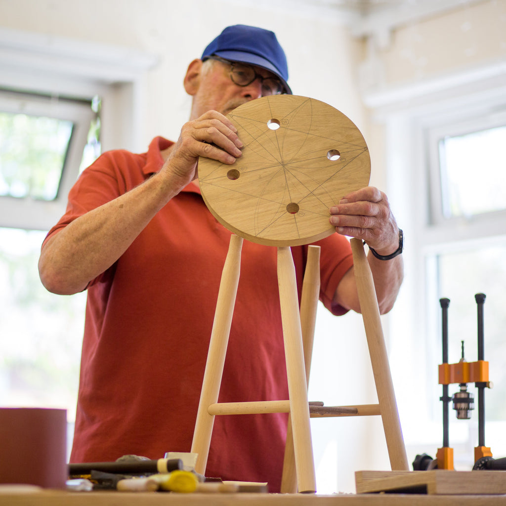 Man in a workshop holding a wooden stool