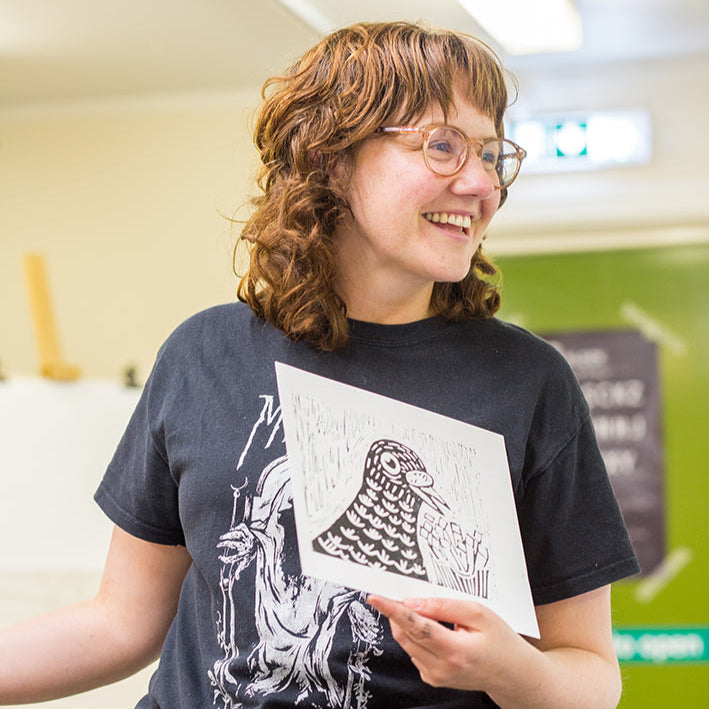 Person wearing a black t-shirt with a graphic design, holding a piece of paper.