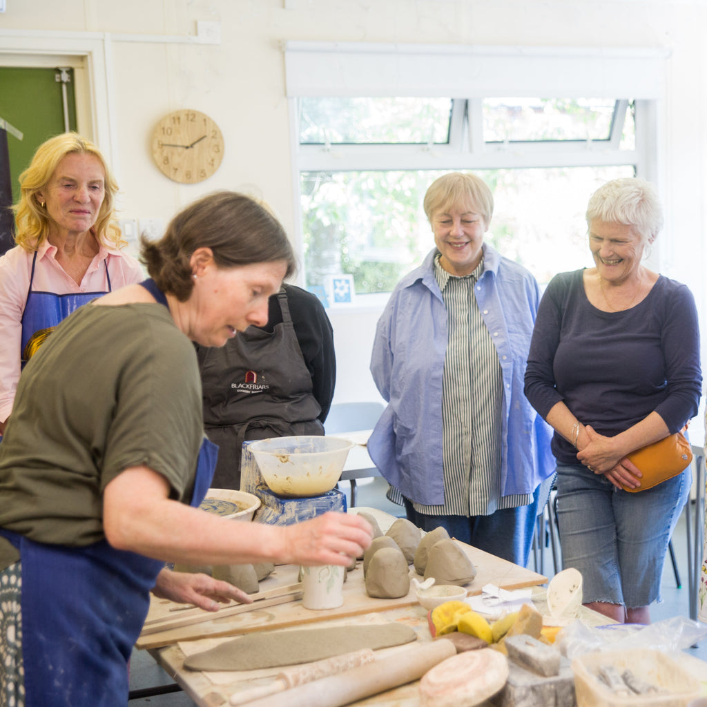 Group of people in a pottery class observing a potter at work.