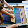 Person using a squeegee to apply ink to a screen printing frame.