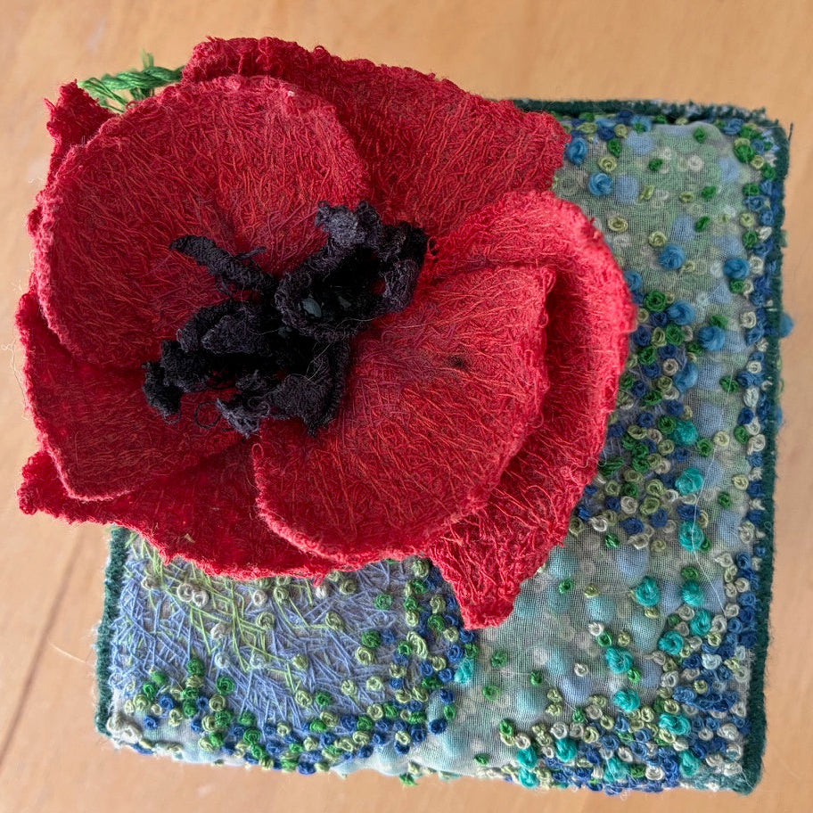 Red flower-shaped object on a textured blue and green fabric background