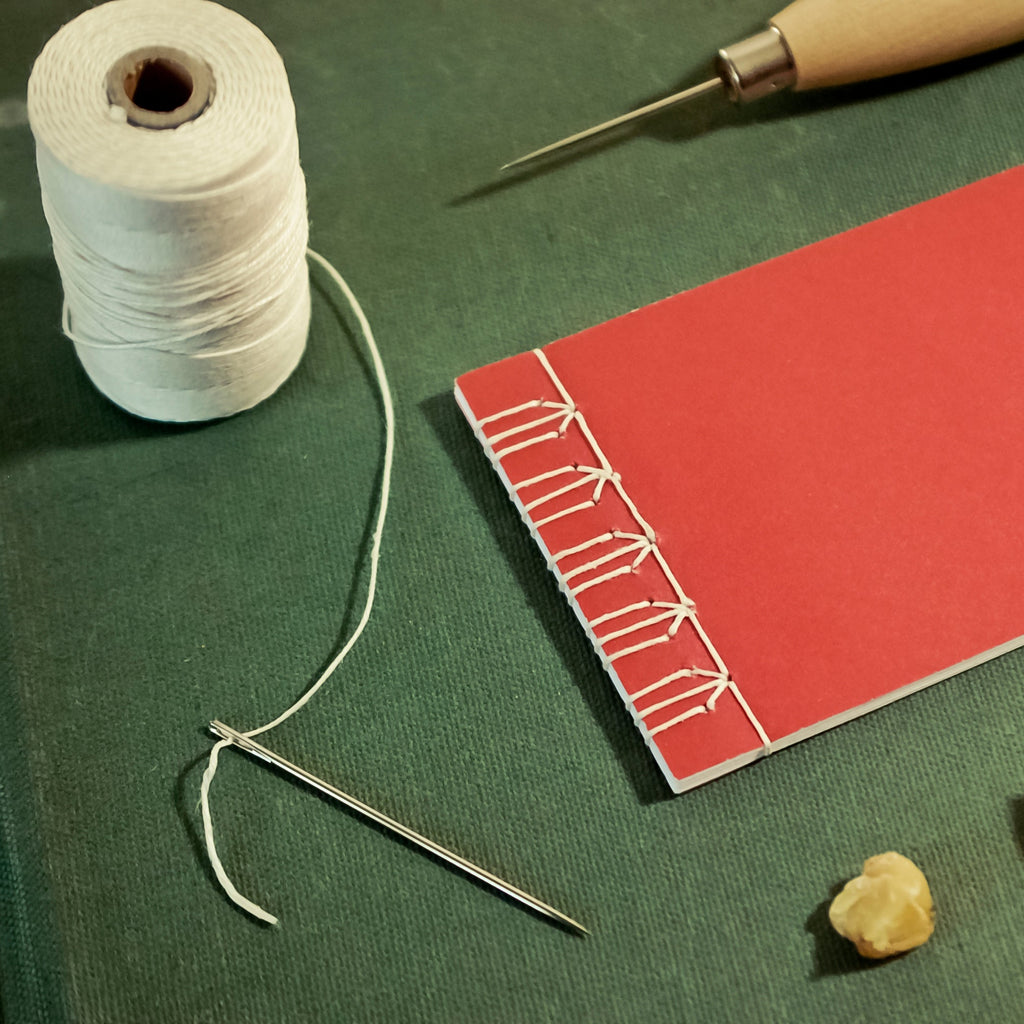 Red notebook with string, needle, and stones on a green surface