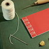 Red notebook with string, needle, and stones on a green surface