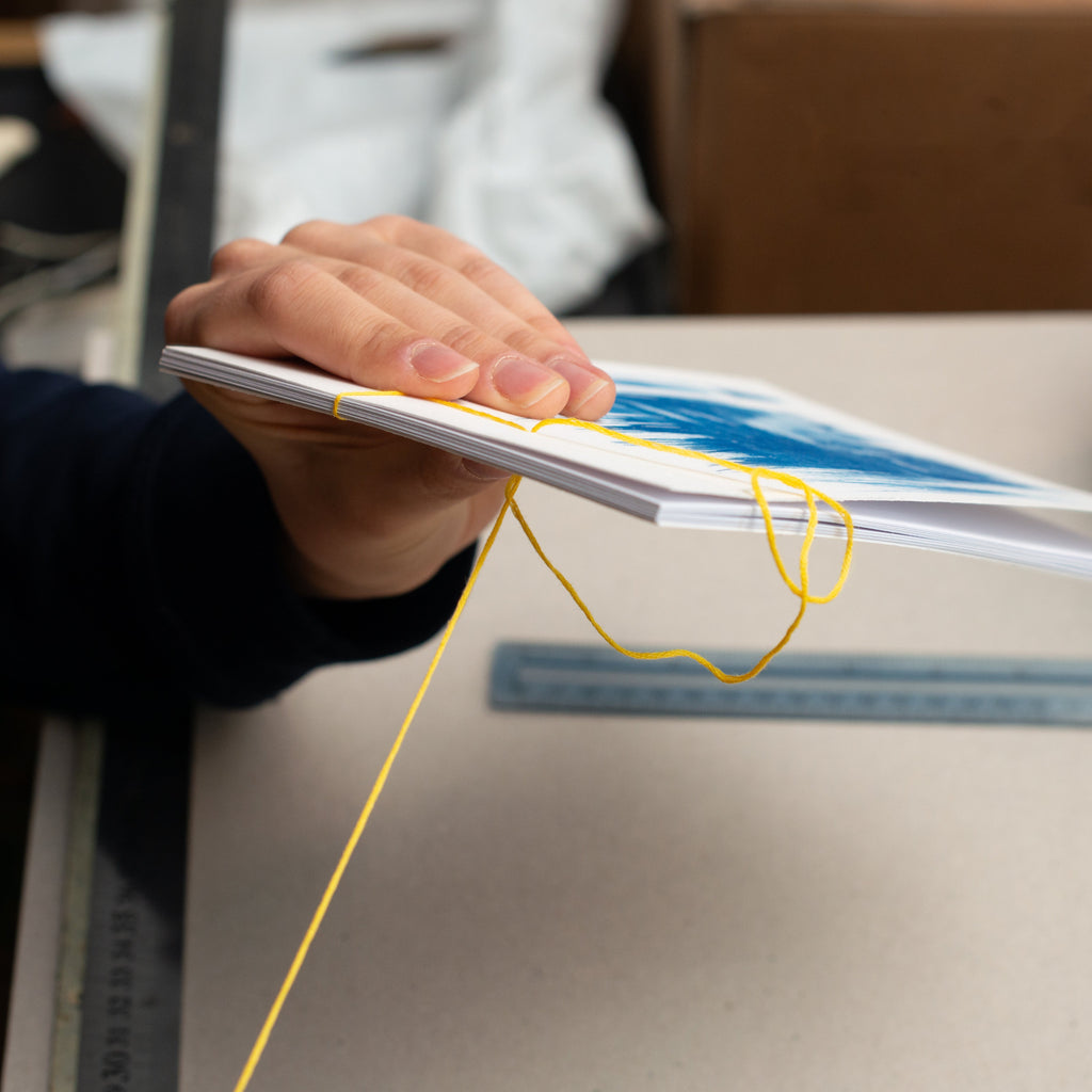 A close-up of a person's hand holding a stack of printed cards or pages bound with a yellow elastic string, with a desk and blue storage box in the background.