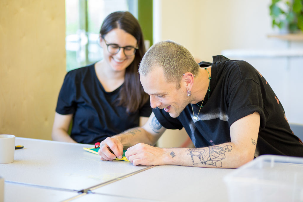 Two people sitting at a table, one of whom is sewing
