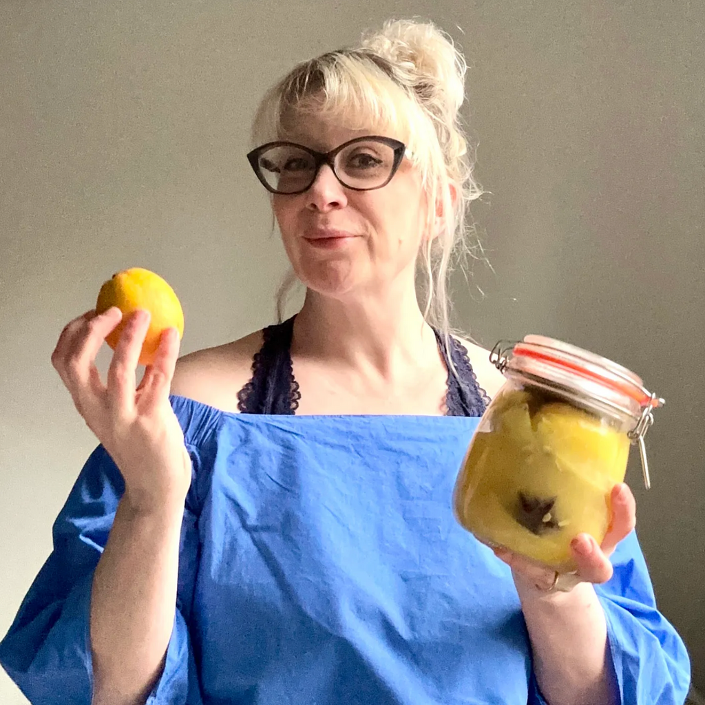 Woman holding a lemon and a jar of pickled apples against a plain background