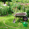 Garden with wheelbarrow, watering can, and tools on a grassy area with flowers and plants.