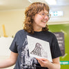 Person wearing a black t-shirt with a graphic design, holding a piece of paper.